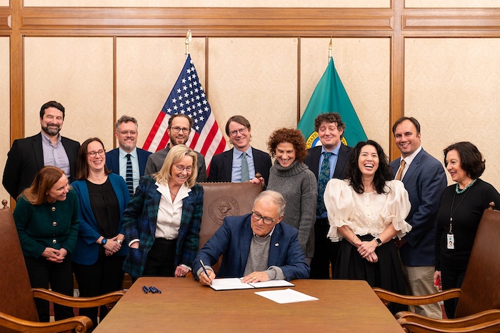 Gov. Jay Inslee signs Executive Order 24-06 to advance salmon recovery and riparian restoration, flanked by advisors and agency directors involved in salmon, clean energy, and habitat.